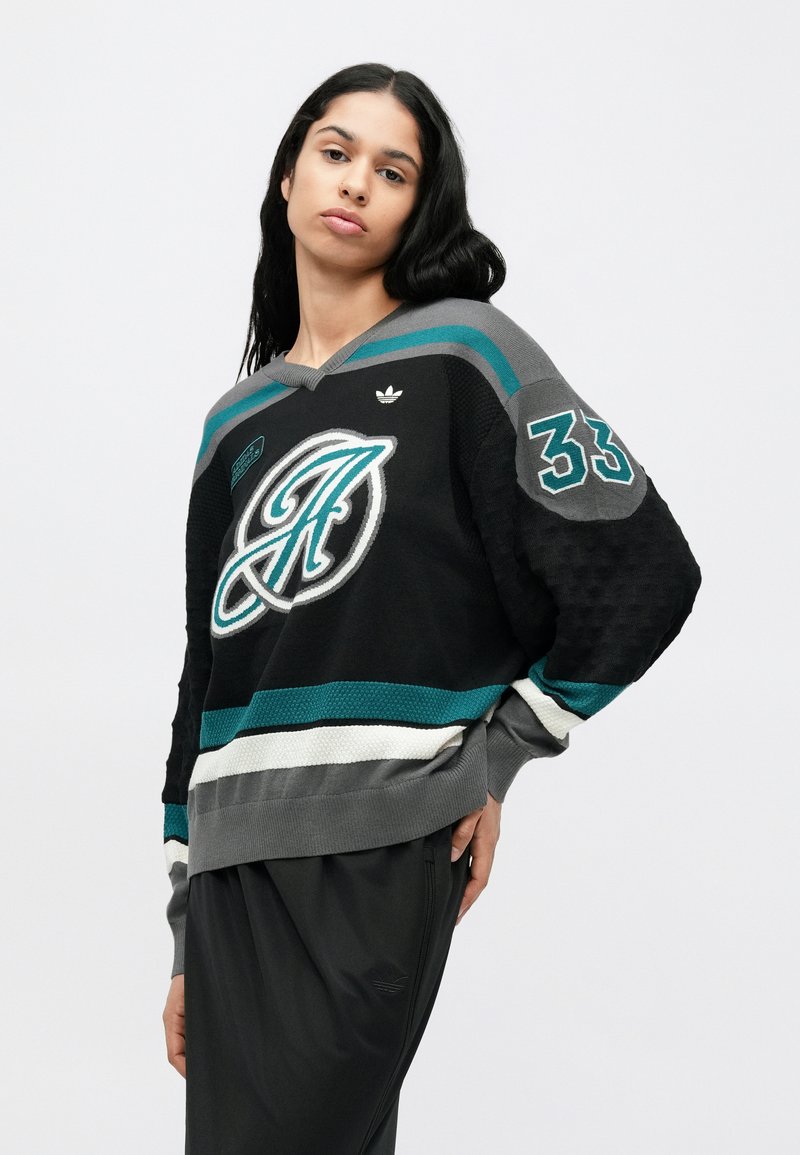 Pull-over noir en tricot avec des rayures bleu sarcelle et grises, avec un grand logo imprimé et le numéro 33 sur la manche. Col et poignets côtelés.