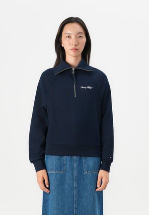 Marineblaue Sweatshirt mit hohem Kragen, Viertel-Reißverschluss und gerippten Bündchen. Mit weißem besticktem Logo auf der Brust und weicher Textur.