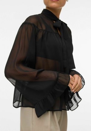Blouse noire semi-transparente avec un col haut et un nœud noué. Présente des manches longues évasées avec des poignets volants et une coupe décontractée.