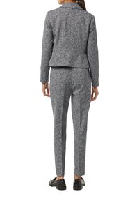 Maßgeschneiderte graue und weiße Hahnentrittmuster-Jacke mit passenden schlanken Hosen. Glattes Textil, Reverskragen und konisch zulaufende Beine. Schwarze Schuhe.