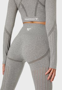 Gray athletic set featuring a fitted long-sleeve top and high-waisted leggings with mesh panels and "SQUATPROOF" logo accents.