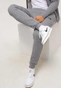 Gray sweatpants made from a soft fabric, featuring elastic cuffs and a small logo patch, paired with white sneakers with black accents.