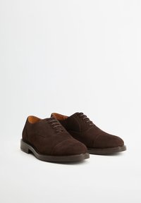 Une paire de chaussures de ville pour hommes en daim marron foncé avec des bouts en cap et des lacets, présentée sur un fond blanc uni.