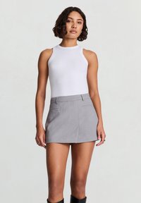 White ribbed tank top with a high neckline paired with a gray mini skirt featuring front pockets, smooth texture, and tailored fit.