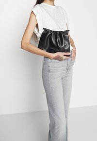 Černá kožená kabelka se shromážděným designem, uzavřená stahovací šňůrou; hladký povrch na pozadí světlého šedého oblečení.