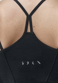 Čierny športový top s dizajnom s ramienkami na chrbte, ryhovanou textúrou a jemným logom umiestneným na zadnom paneli.