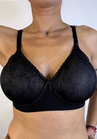 Sostenedor negro con patrón floral texturizado, con encaje en el borde superior, tirantes ajustables y un detalle de lazo en la parte frontal central.
