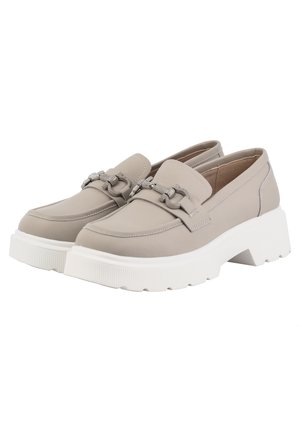 Femme portant un blazer beige oversize, un short assorti jusqu’au genou, un crop top blanc, un collier argenté épais et des mocassins à plateforme beiges.