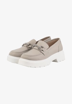 Femme portant un blazer beige oversize, un short assorti jusqu’au genou, un crop top blanc, un collier argenté épais et des mocassins à plateforme beiges.