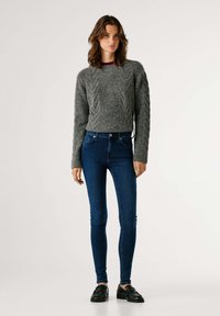 Suéter gris con textura, de manga larga, combinado con vaqueros ajustados azules y zapatos negros. Diseño sencillo, tela suave, forma ajustada.