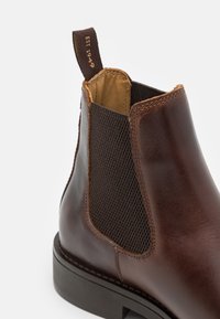 Brauner Lederstiefel mit elastischen seitlichen Einsätzen, strukturiertem Stoff und Zuglasche. Mit gerundeter Zehenpartie und robustem Außensohlen. 