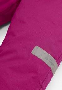 Fliisisis voodriga jakk erksas magenta kangas, millel on hall sildikujundus reljeefse tekstiga. Sile tekstuur ja eristuv värviküllus.