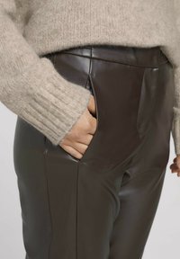 Bruna fuskläderbyxor med sidofickor, visade med en ljusbeige stickad tröja. Texturerad tyg med en slät yta.