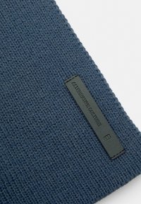 Gebreide marineblauwe stof met een textuur patroon, voorzien van een zwart leren label met de inscriptie "ALTERNATIVE CULTURE."