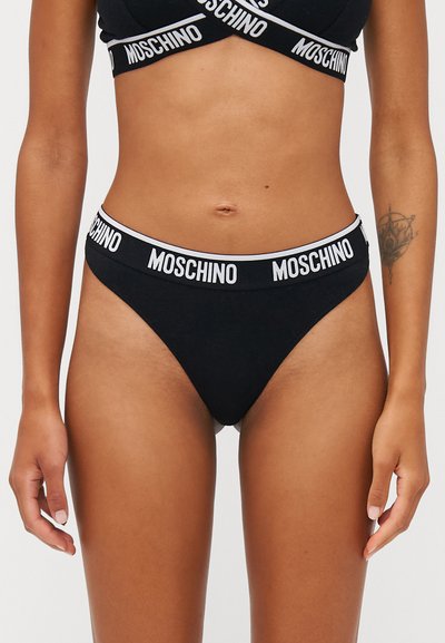 Schwarzer Baumwolltanga mit einem elastischen Bund, der mit dem weißen "MOSCHINO"-Logo verziert ist. Glatte Textur, minimalistisches Design und hoher Beinausschnitt.