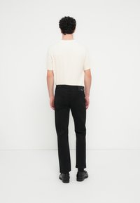 Μαύρο παντελόνι και μπλούζα κρεμ χρώματος που φαίνονται από πίσω. Η μπλούζα έχει κοντά μανίκια και το παντελόνι έχει κανονική εφαρμογή με πίσω τσέπες.