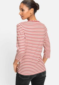 Red and white striped long-sleeve top with a round neckline and three-quarter sleeves, made from a soft fabric, paired with dark jeans.