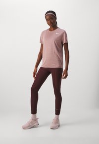 Nike spordirõivad: lühikeste varrukatega, heleda roosa heegeldatud t-särk, burgundi värvi legginsid külgseemnetega ja heleda roosa tossud valgete aktsentidega.