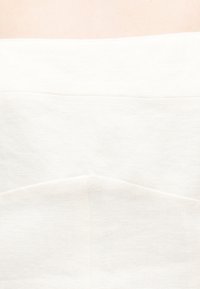 Τρία διπλωμένα λευκά πλεκτά πουλόβερ στοιβαγμένα πάνω σε επιφάνεια ανοιχτού ροζ χρώματος, που δείχνουν την υφή και τις ραφές.