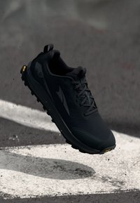 Chaussure de trail running noire avec une tige texturée, un système de laçage et une semelle rembourrée. Accents en Vibram sur la semelle extérieure pour l'adhérence et la durabilité.