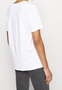 Hvid bomulds t-shirt med korte ærmer, afslappet pasform, rund halsudskæring og glat tekstur, vist fra en trekvart bagfra vinkel.