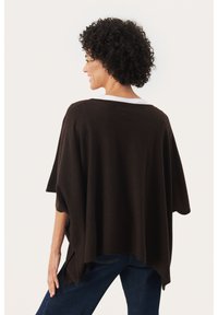 Poncho en tricot marron avec une coupe large et décontractée, présentant un col rond et des fentes sur les côtés, associé à un jean bleu foncé. Texture douce.