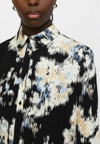 Zwart-witte blouse met een patroon van blauwe en beige abstracte vormen, uitgerust met een klassieke kraag en knoopsluiting. Glad stofontwerp.