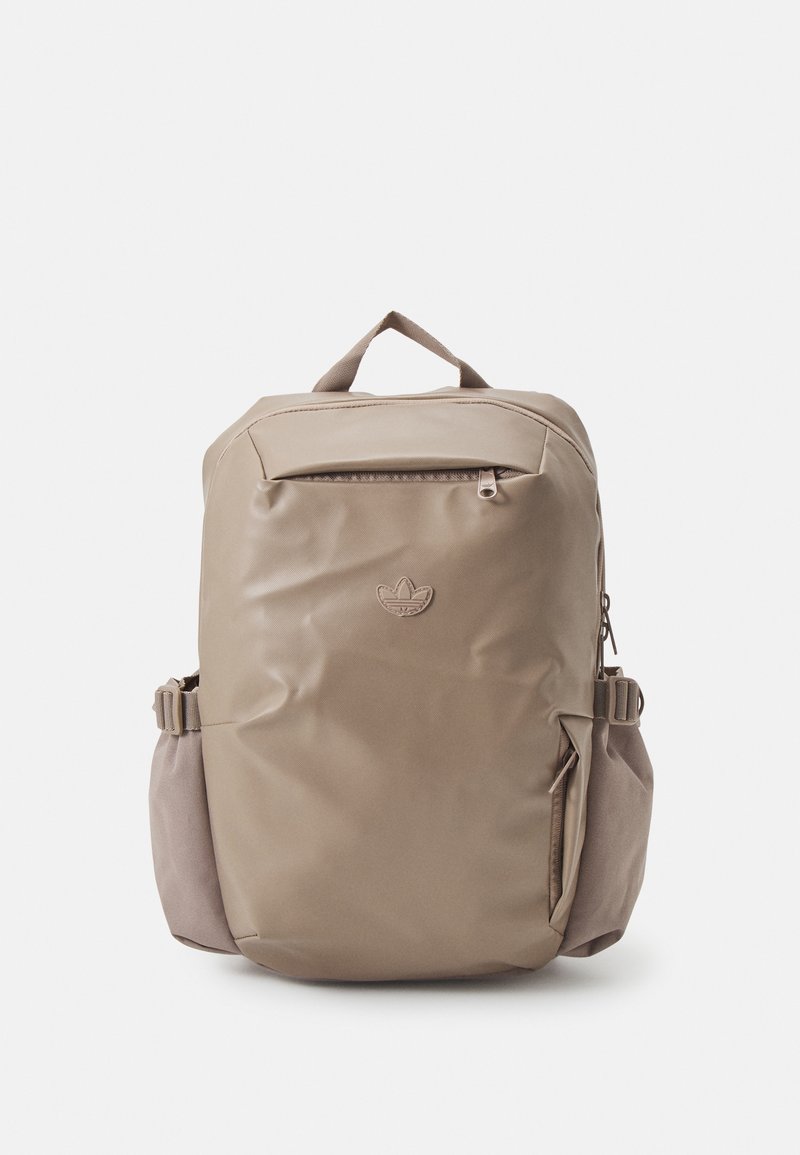 Mochila beige con un acabado brillante, que cuenta con un bolsillo con cremallera en la parte frontal, un bolsillo lateral decorativo y una asa en la parte superior para llevar.