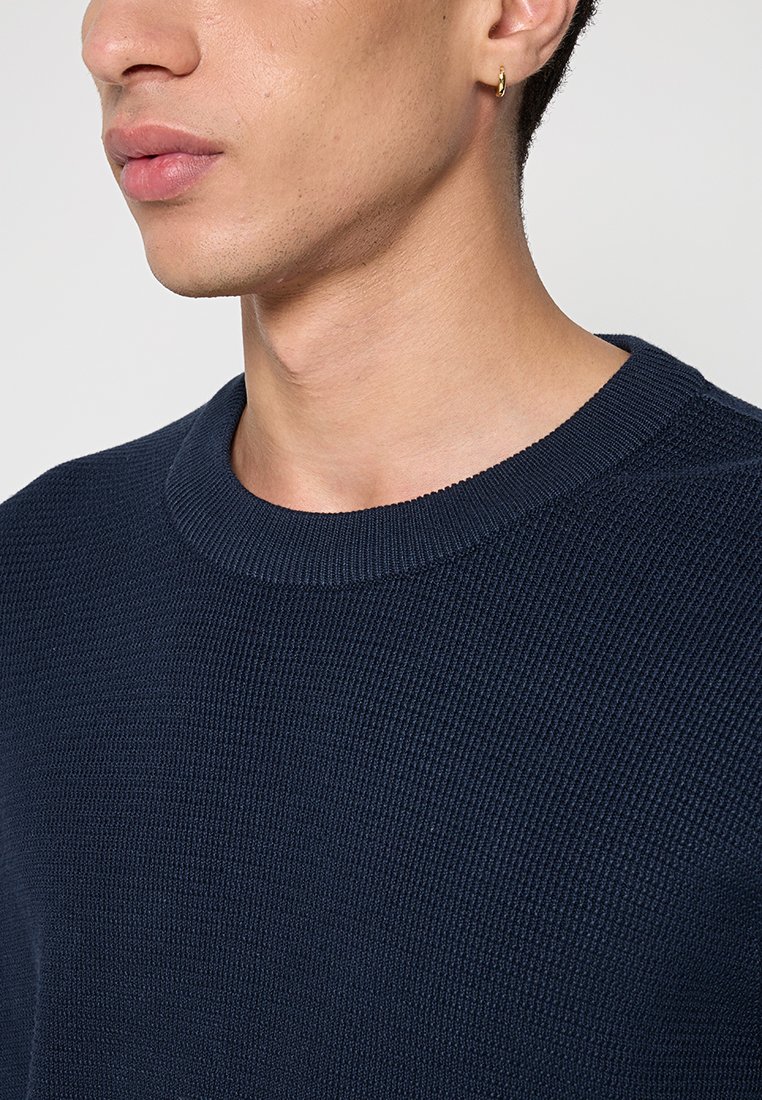Marineblauer Strickpullover mit gerippter Textur und Rundhalsausschnitt. Nahaufnahme, die Details des Stoffes und des Kragen Designs zeigt.