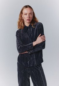 Sötétkék, mintás ing gombos elüls�ő résszel, klasszikus gallérral és hosszú ujjal. Az anyag függőleges csíkokat tartalmaz, és laza szabású.