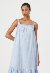 Svetlomodré a biele pruhované šaty s nariaseným výstrihom, ramienkami na tenké pásiky a volánovým lemom. Vyrobené z ľahkej tkaniny.