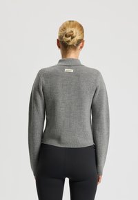 Grijze geribde trui met een kraaghalslijn en een merklabel aan de achterkant. Lange mouwen, aansluitend ontwerp en textiel met een textuur.