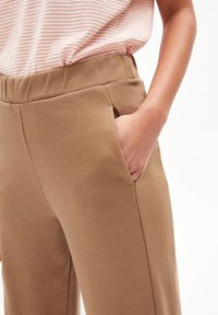 Pantalons stretch beiges avec une texture lisse, dotés de poches latérales et d'une large taille élastique. Associés à un haut à rayures à manches courtes.