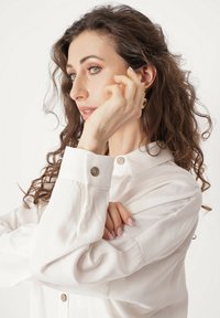 Biała koszula z długimi, zwiewnymi rękawami i kołnierzykiem. Posiada ozdobny guzik przy mankiecie oraz gładką, miękką fakturę.