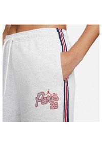 Graue Baumwoll-Jogginghosen mit roten und blauen Seitenstreifen, einer Tasche und "Paris 23" in roter Stickerei mit einem Logo-Akzent darüber.