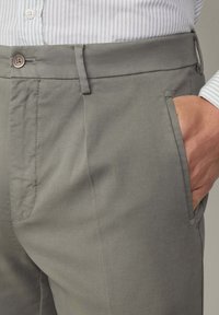 Graue Chinos aus robustem Stoff, ausgestattet mit Seitentaschen, einem Knopfverschluss und einer glatten Oberfläche. Sichtbare Nahtdetails am Bund.