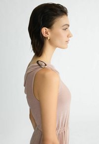 Roze mouwloze jurk met een gestructureerde afwerking, heeft een geraffineerde halslijn en een gouden accent op de schouder. Glad materiaal met een zachte glans.