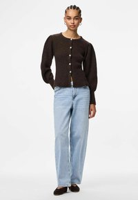 Brūns adīts kardigans ar pūkainām piedurknēm, ar sudraba pogu aizdari, salikts ar gaiši zilām platām biksēm un brūnām kurpēm.