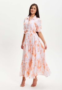 Maxi dress in white with orange tie-dye patterns, featuring a button-up collar, puffed sleeves, and ruffled hem accents for texture.