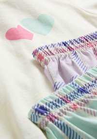 Top en coton avec deux cœurs imprimés. Présente des bretelles froncées dans des couleurs pastel : lilas avec des rayures et menthe avec un motif multicolore.