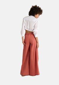 White cropped shirt with long sleeves paired with loose, rust-colored wide-leg trousers featuring an elastic waistband.