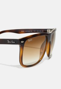 Ochelari de soare Ray-Ban cu ramă din fâșie de broască țestoasă, lentile maro cu gradient și accente argintii pe laturi. Formă clasică pătrată și finisaj lucios.