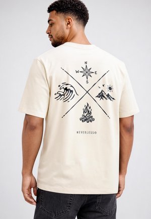 Man wearing a beige t-shirt with black graphic of compass, ocean wave, campfire, mountains, sun, birds, and "NEVERLESS" text on the back.