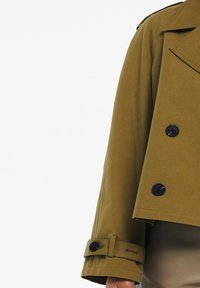 Giacca corta verde oliva con colletto a revers, bottoni doppi e polsini regolabili. Tessuto liscio e design casual e strutturato.