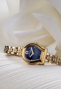 Guldtonad klocka med en tårformad blå urtavla, silvertonad armband med länkdesign, utrustad med ett spänne och varumärkeslogotyp.