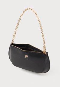 Juodas odinis rankinukas su auksine grandinėlės dirželiu ir užtrauktuko uždarymu. Priekyje yra logotipo emblema, o paviršius yra lygus.