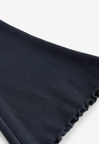 Gros plan sur un tissu côtelé foncé avec un ourlet flottant sur un fond uni clair.