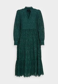 Grön spetsklänning med långa ärmar, en vågig halsringning, en lager-på-lager kjol och intrikata utskärningar genom hela klänningen.