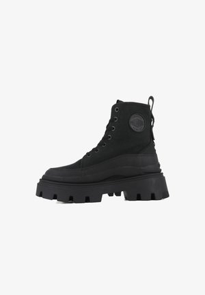 Black high-top boots with a chunky sole, featuring a canvas upper, rubber accents, six eyelets, and a branded circular patch.