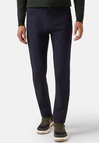 Pantalones elásticos en color marino con corte recto, que cuentan con bolsillos frontales y una textura suave, combinados con zapatillas oscuras.